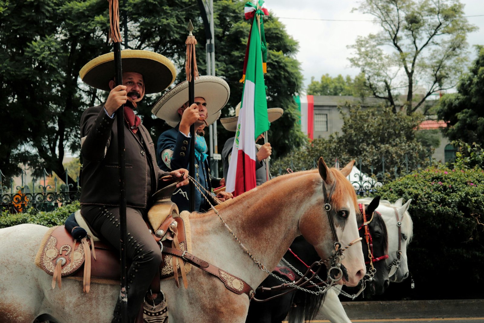 Charros in traditional attire riding horses during a parade in Ciudad de México.